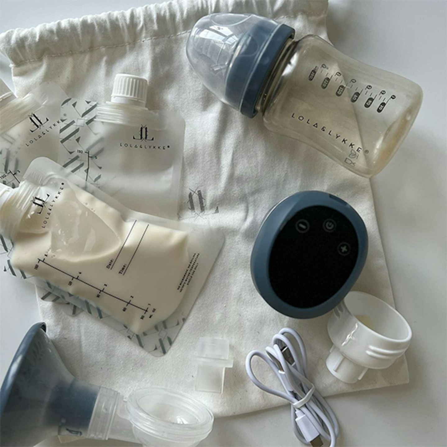 Lola and Lykke Smart Electric Breast Pump, taken apart and lying on a soft bag, with a storage pouch of milk