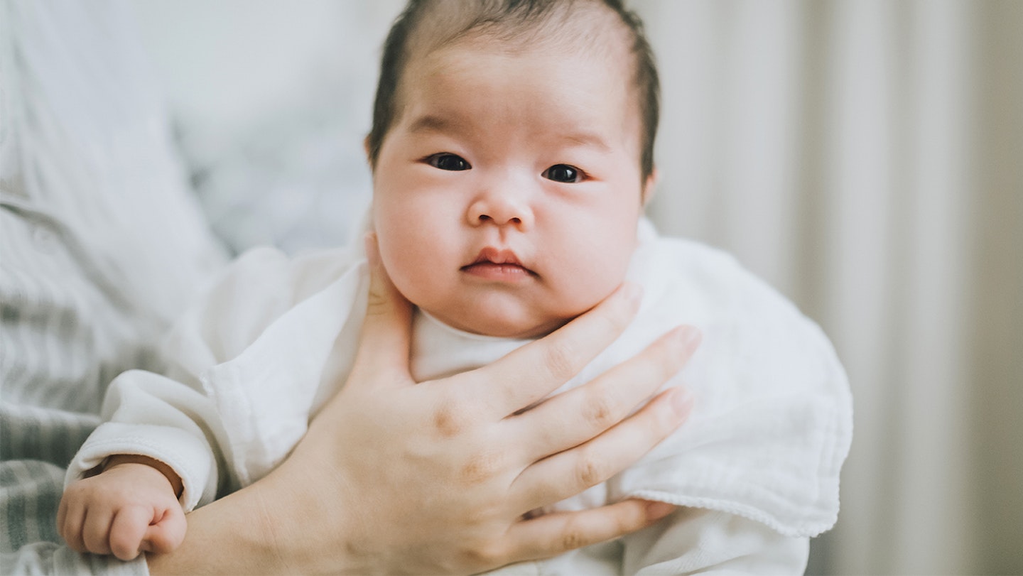 A baby sitting upend facing the camera, being burped